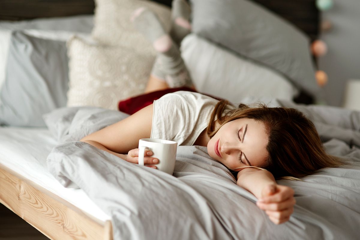 Eine Frau liegt mit einer Tasse Tee im Bett