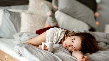 Eine Frau liegt mit einer Tasse Tee im Bett - Foto: iStock_gpointstudio