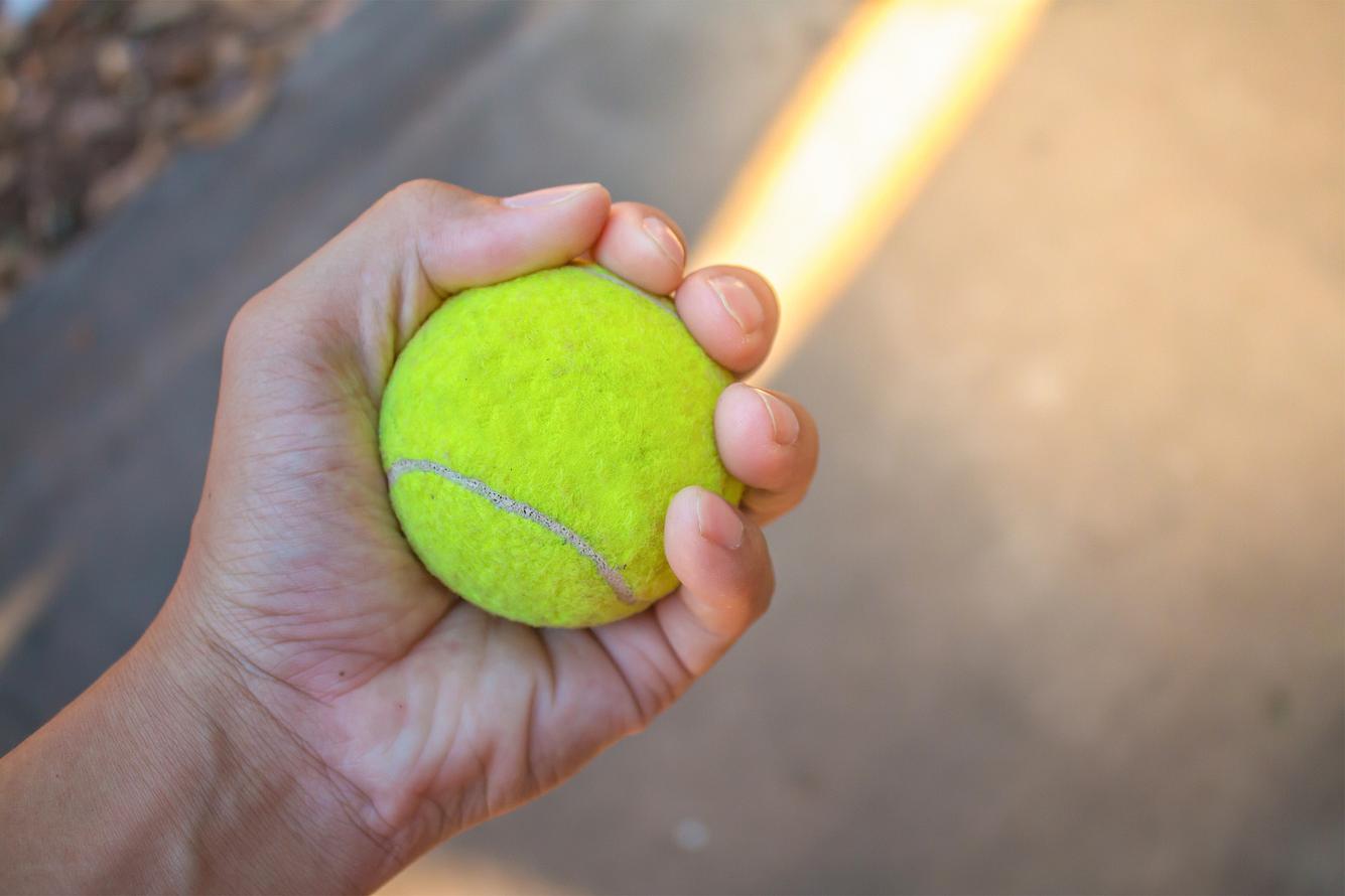 Eine linke Hand presst einen Tennisball