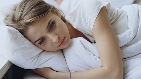 Eine Frau liegt mit geöffneten Augen im Bett - Foto: iStock/silverkblack