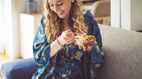 Eine Frau isst Müsli auf dem Sofa - Foto: iStock/Eva-Katalin