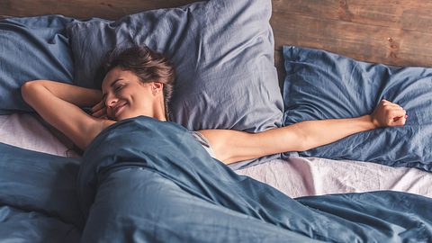 Eine Frau streckt sich im Bett - Foto: iStock/GeorgeRudy