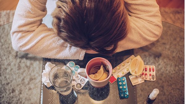 Frau liegt mit Kopf auf verschränkten Armen auf dem Tisch mit Medikamenten um sie herum - Foto: iStock/South_agency