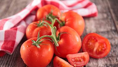 Frische Tomaten und ein kariertes Tuch auf einem Holzuntergrund - Foto: iStock/margouillatphotos