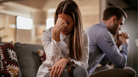 Eine Frau und ein Mann sitzen voneinander abgewendet auf dem Sofa - Foto: istock_Milos Dimic