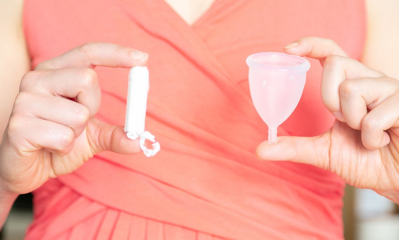 Frau mit TSS hält Tampon und Menstruationstasse in der Hand