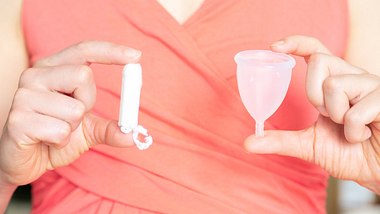 Frau mit TSS hält Tampon und Menstruationstasse in der Hand - Foto: iStock/a_namenko