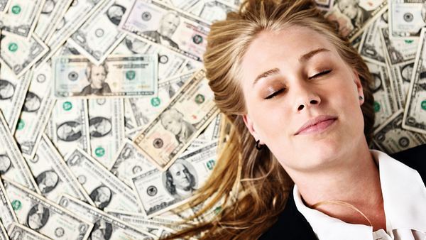 Frau hat Augen geschlossen und liegt auf Dollar-Geldscheinen - Foto: iStock/RapidEye