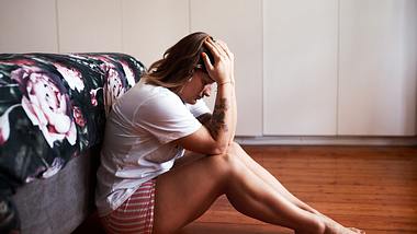 Frau sitzt auf dem Boden und stützt den Kopf in die Hände - Foto:  iStock/PeopleImages
