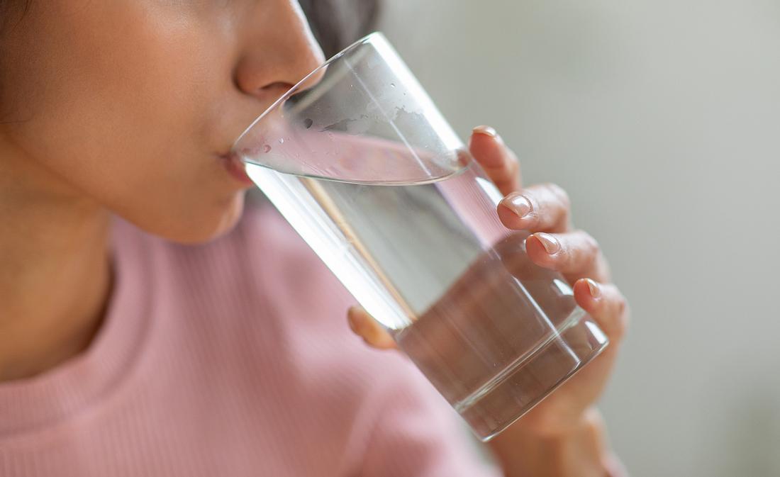Eine Frau trinkt Wasser aus einem großen Glas. 