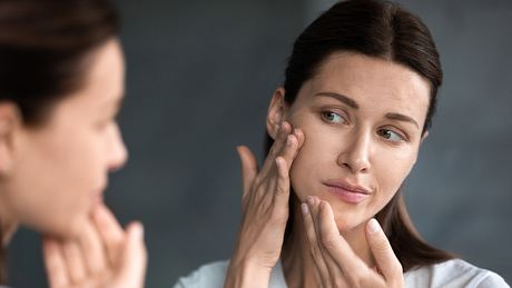 Eine Frau begutachtet ihre trockene Haut im Gesicht im Spiegel - Foto: iStock_fizkes
