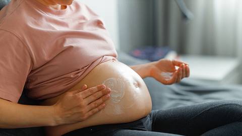 Eine schwangere Frau cremt sich ihren Bauch ein. - Foto: iStock/Georgijevic