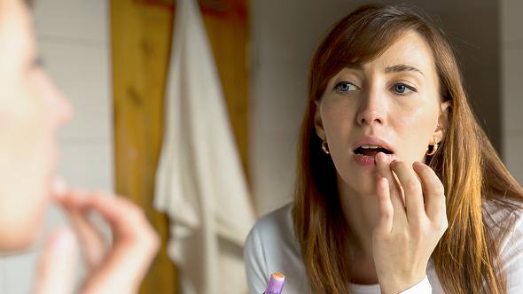 Eine Frau cremt sich die Lippen ein - Foto: iStock/artursfoto