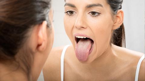 Eine Frau streckt vor einem Spiegel ihre Zunge raus - Foto: istock_4FR