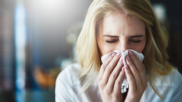 Eine Frau niest in ein Taschentuch - Foto: iStock/PeopleImages