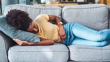 Eine Frau liegt mit Unterleibschmerzen auf der Couch - Foto: iStock / Moyo Studio