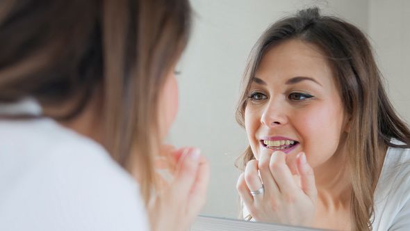 Eine Frau betrachtet ihre Zähne im Spiegel - Foto: iStock/Vesna Andjic