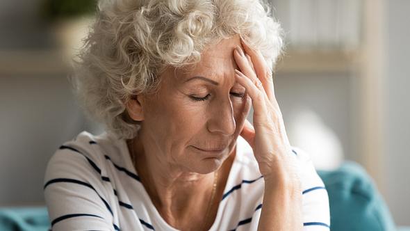 Ältere Frau mit grauen Locken und geschlossenen Augen fasst sich an den Kopf - Foto: iStock/fizkes