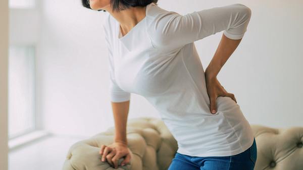 Frau stützt sich mit einer Hand ab und fässt sich mit der anderenan den Rücken - Foto:  iStock/Povozniuk