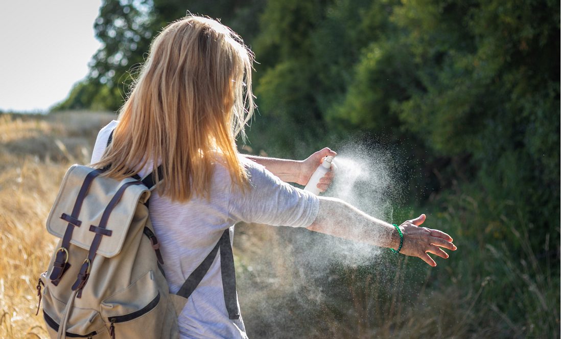 Eine Frau sprüht sich mit Mückenspray ein