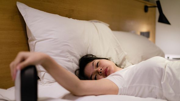 Müde Frau im Bett schaut auf den Wecker - Foto: iStock/rudi_suardi