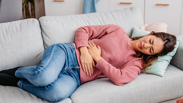 Frau hat Völlegefühl nach dem Essen und liegt auf dem Sofa - Foto: iStock/urbazon