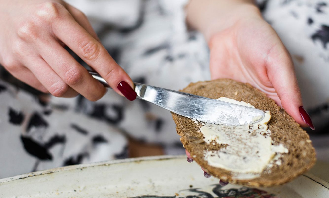 Frau schmiert Butter auf Vollkornbrot