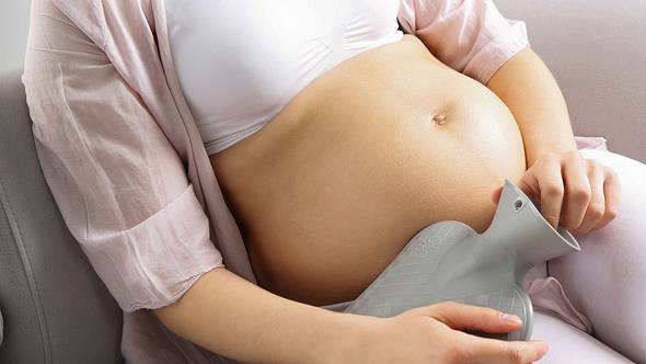 Schwangere hält Wärmflasche an Bauch - Foto: IMAGO/YAY Images