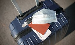 Ein Koffer, auf dem ein Reisepass und eine Mundschutzmaske liegen - Foto: istock/elenaleonova