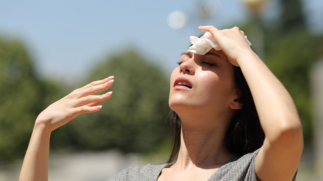 Frau hält sich nasses Tuch auf die Stirn gegen Hitze. - Foto: iStock / Pheelings Media