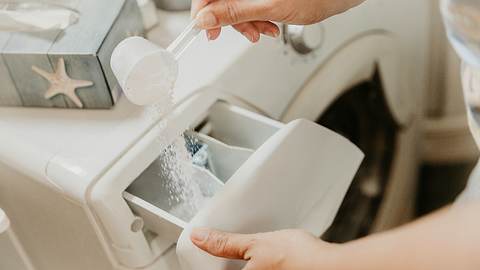Eine Frau füllt Waschpulver in eine Waschmaschine - Foto: iStock / SimonSkafar