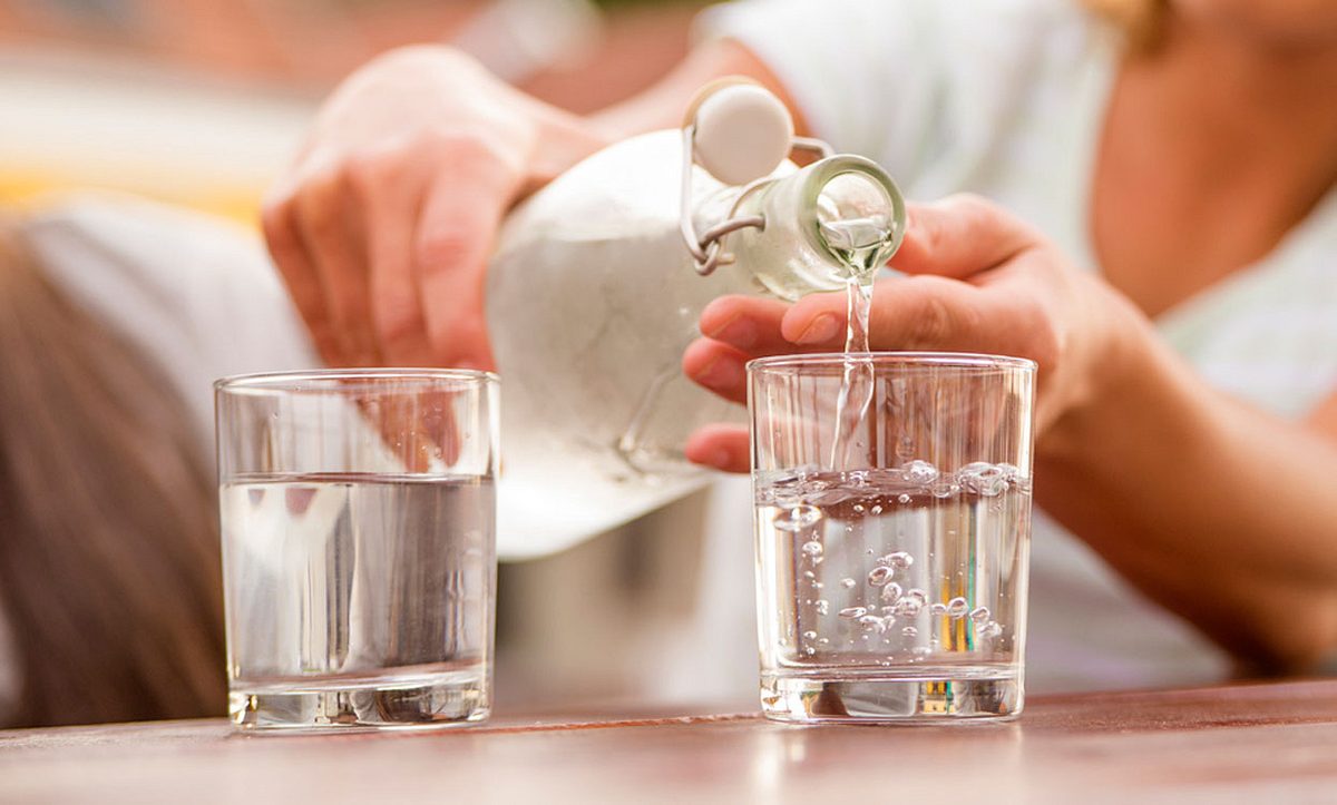 Frau schenkt im Garten Wasser in ein Glas ein