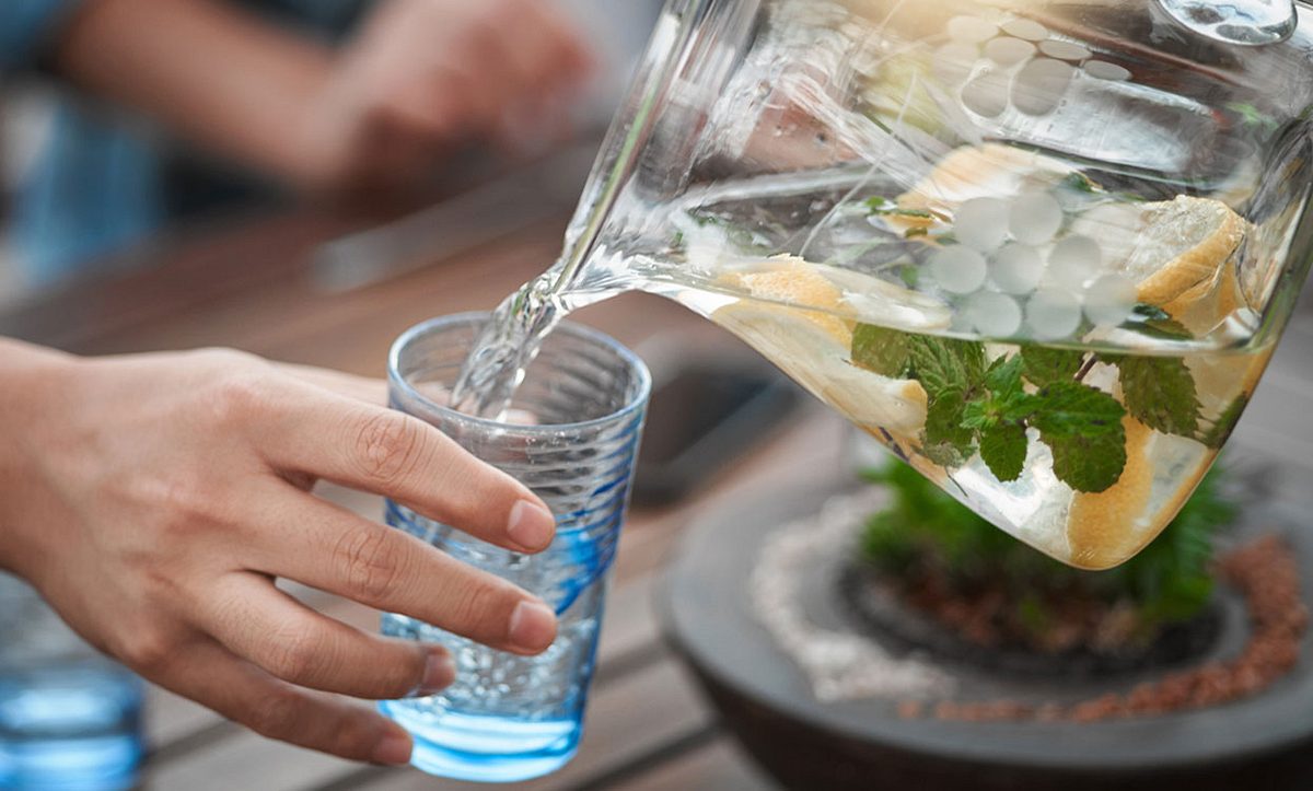Wasser mit Minzblättern aus Karaffe in ein Glas schütten