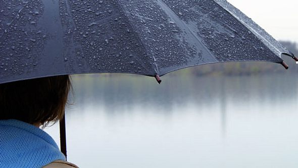 Eine Frau steht mit einem Regenschirm an einem See - Foto: Fotolia