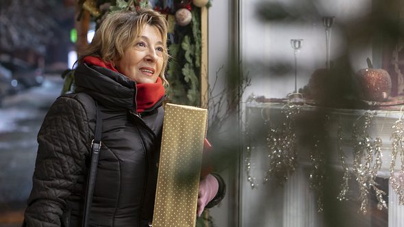 Eine ältere Frau steht mit einem Paket in der Hand vor einem Schaufenster - Foto: iStock/BakiBG