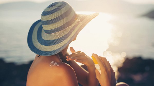 Eine Frau mit einem Hut cremt sich mit Sonnencreme ein - Foto: iStock/Jovanmandic