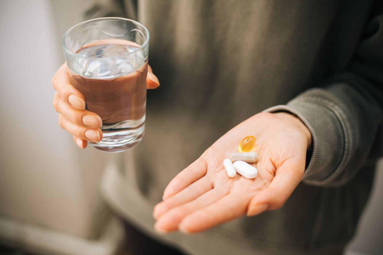 Eine Person hält in der einen Hand ein Wasserglas und in der anderen verschiedene Tabletten