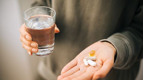 Eine Person hält in der einen Hand ein Wasserglas und in der anderen verschiedene Tabletten - Foto: iStock/agrobacter