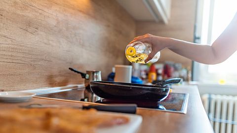 Eine Frau gießt Öl in eine Pfanne auf dem Herd - Foto: iStock-1135949260 ljubaphoto