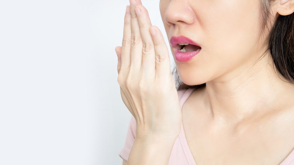 Person hält sich Hand vor das Gesicht und testet Atem - Foto: Istock/Nitcharee Sukhontapirom