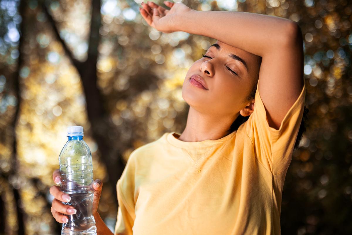 Frau mit Wasserflasche legt sich den Arm an die Stirn