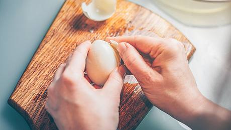 Frau schält ein Ei. - Foto: iStock/ andreygonchar