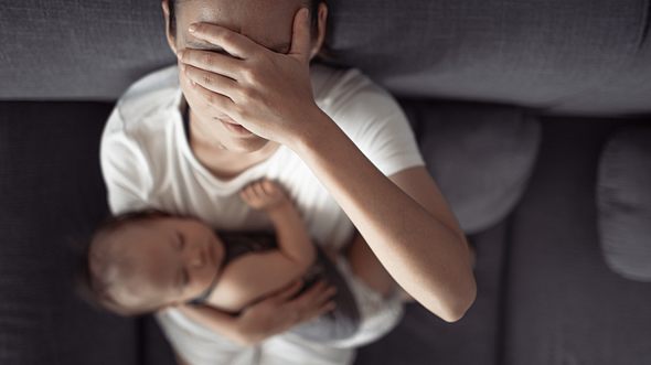 Eine Mutter mit Baby im Arm fasst sich an den Kopf - Foto: iStock/kieferpix