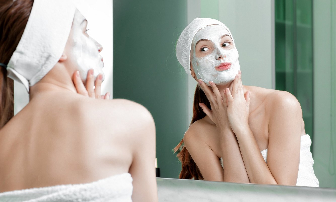 Frau mit Gesichtsmaske schaut sich im Spiegel an