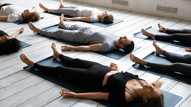 Yogagruppe in entspannter Rückenlage auf Matten auf einem Holzfußboden - Foto: iStock-ID 1199687510 fizkes