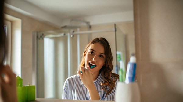 Eine Frau putzt sich die Zähne und guckt dabei in den Spiegel - Foto: istock_bernardbodo
