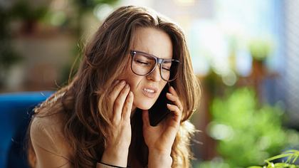 Frau mit Zahnschmerzen telefoniert - Foto: iStock/CentralITAlliance
