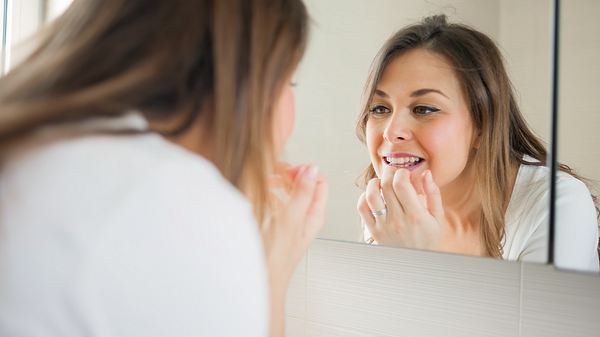 Frau betrachtet ihre Zähne im Spiegel. - Foto: iStock/Vesna Andjic