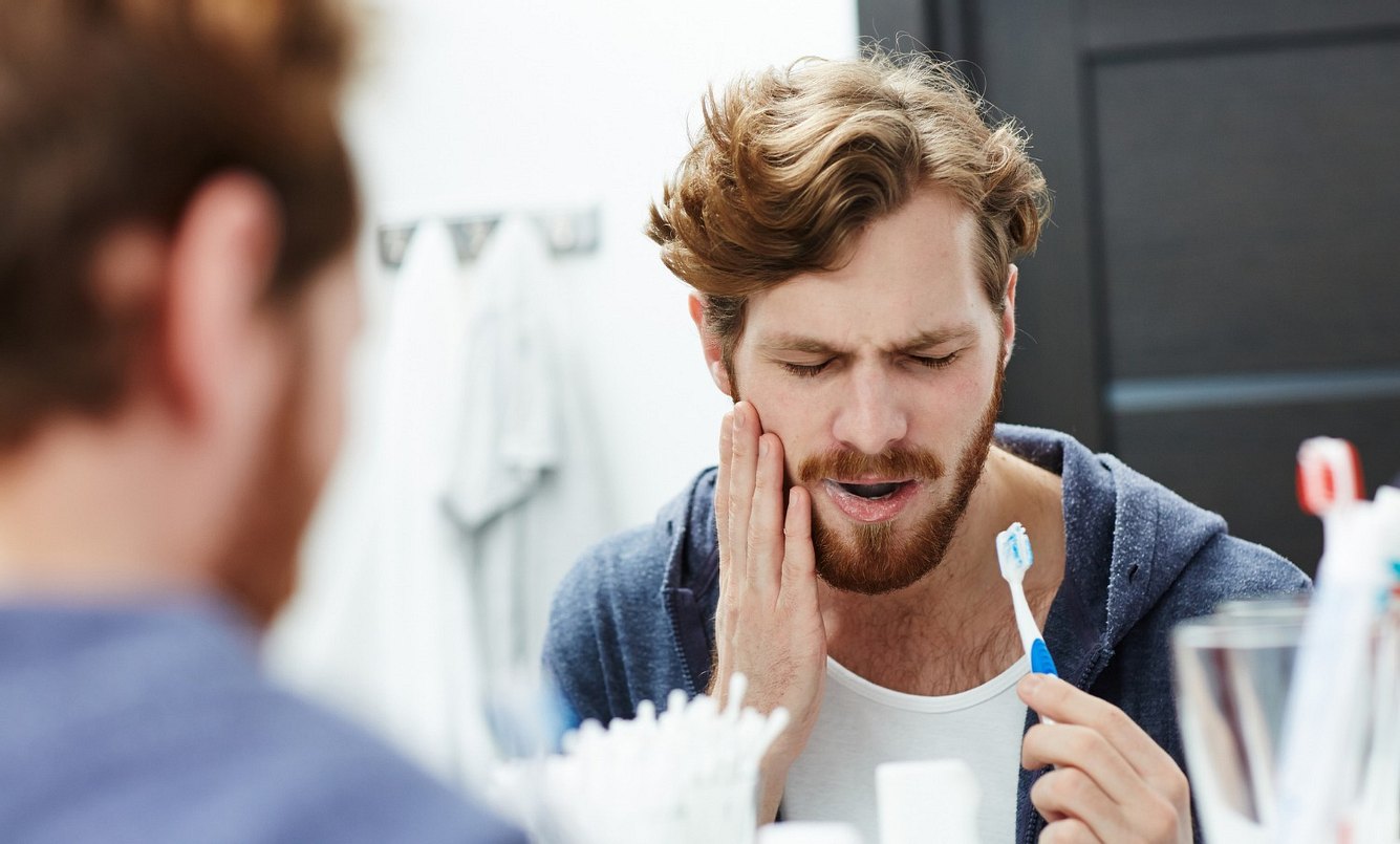 Junger Mann putzt sich die Zähne und hat Schmerzen wegen Zahnwurzelentzündung