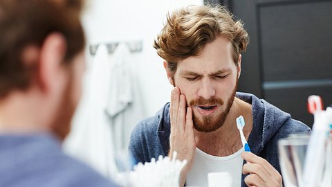 Junger Mann putzt sich die Zähne und hat Schmerzen wegen Zahnwurzelentzündung - Foto: shironosov/iStock